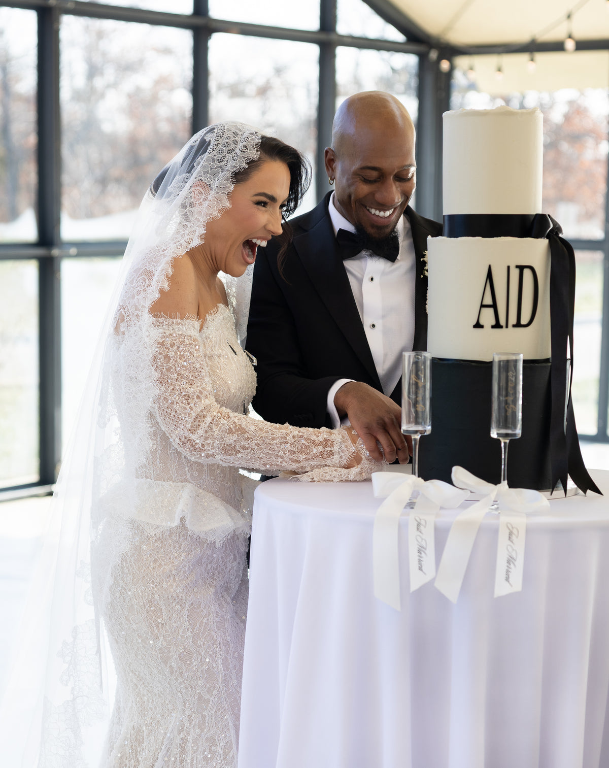 Couple cutting a wedding cake with engraved champagne glasses for toasting.