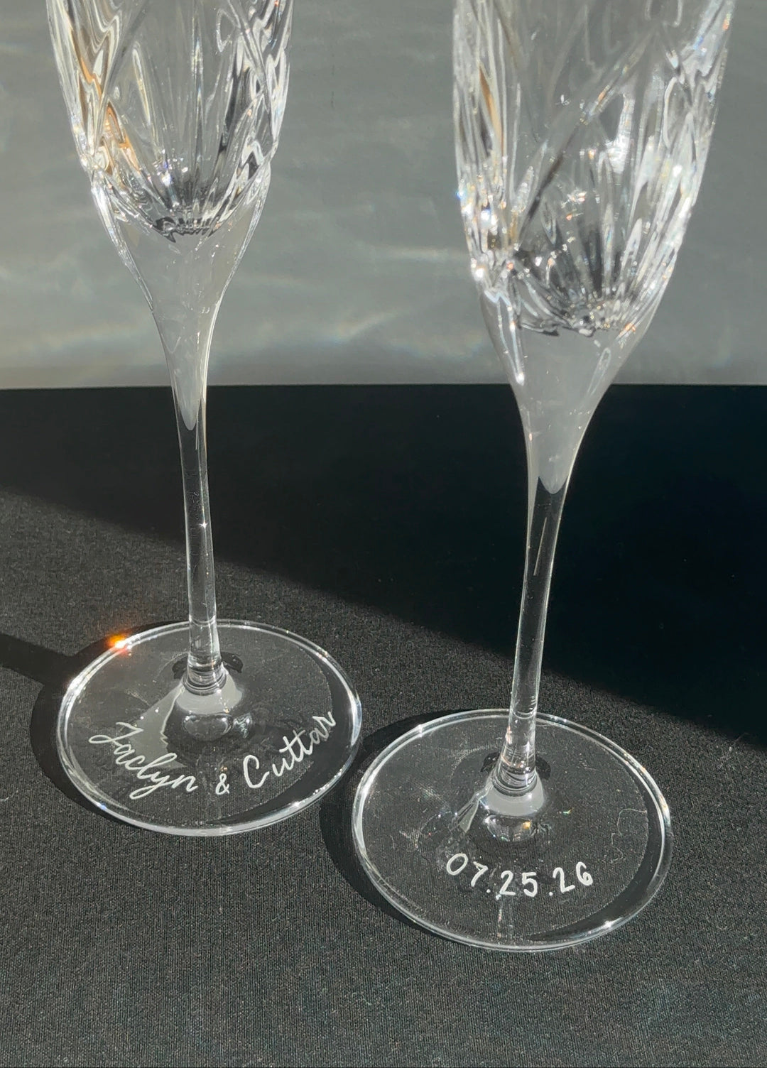 Two crystal champagne flutes with engraved names and dates on a dark surface. Wedding day keepsake created in Kansas City. 